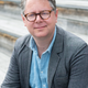 Photo of Financial Times journalist Robin Wigglesworth, sitting on steps and wearing a button-down shirt and grey jacket.